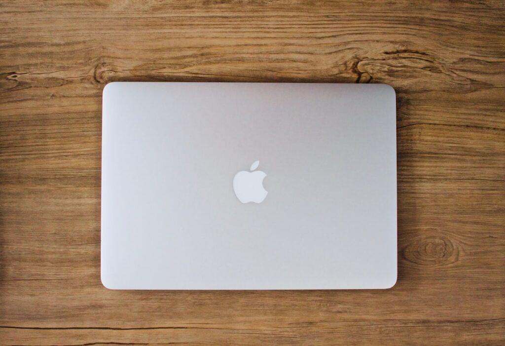 MacBook Ultraは思ったより高くなるのか? miniLED版MacBook Proが2028年まで併売との報道、2,499ドルと2,999ドルの2段構えか【海外ニュース】 – Smart Watch Life|スマートウォッチとガジェットのデジタル活用専門メディア 木製のデスクに置かれた閉じたMacBookを真上から写したイメージ画像