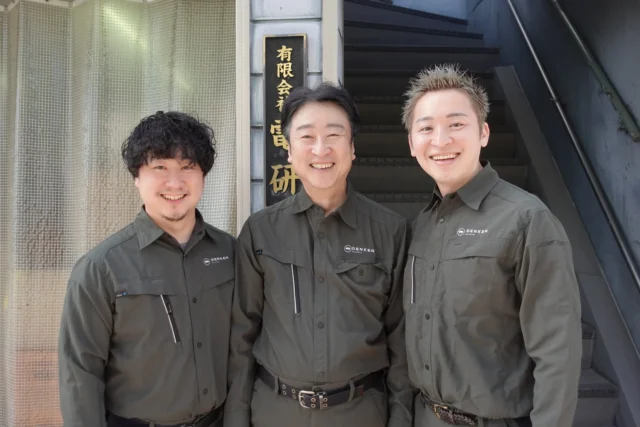 有限会社電研の作業着を着た3人の男性が笑顔で並ぶ集合写真