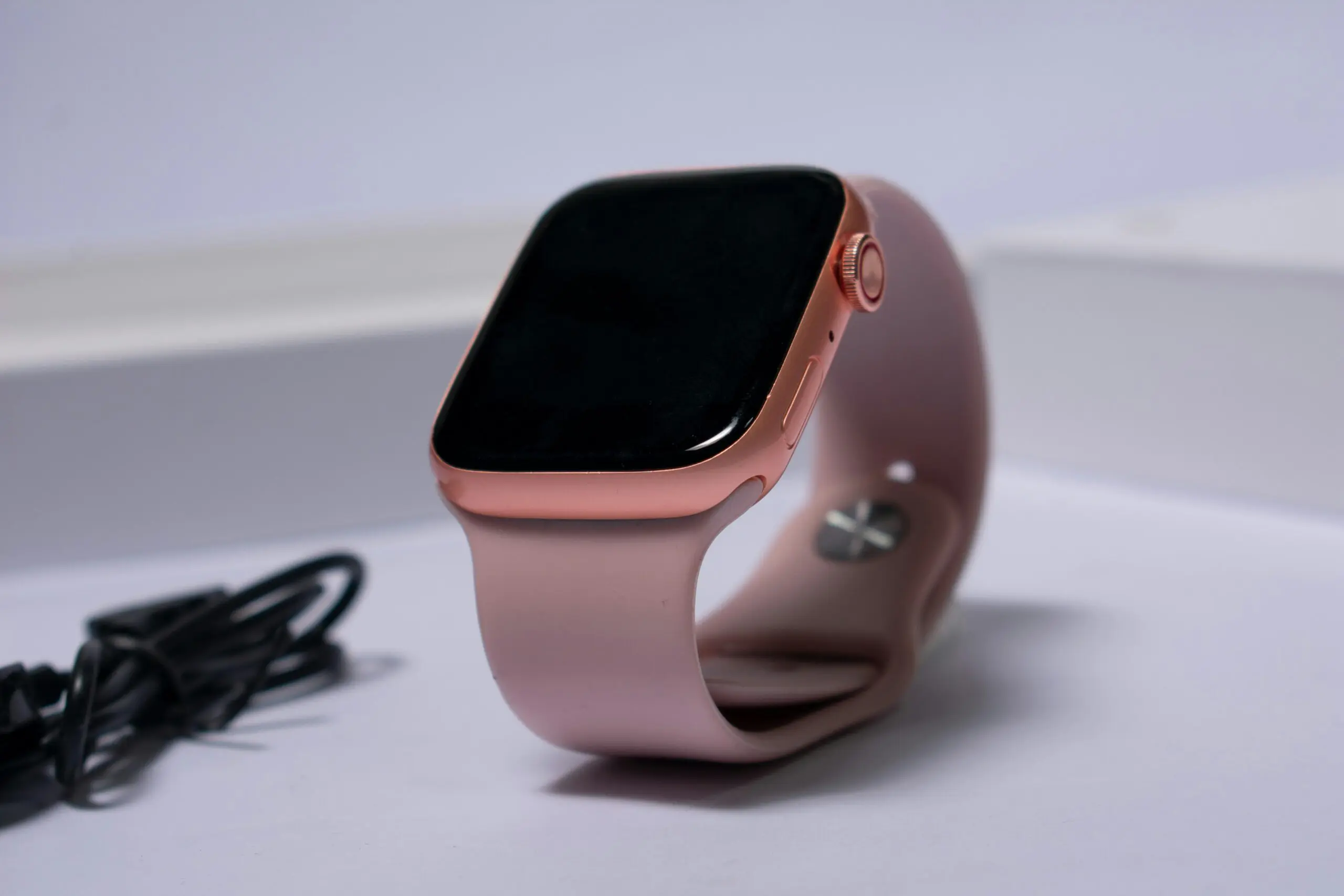ライトパープルの背景に置かれたピンクのApple Watch。画面は消灯している