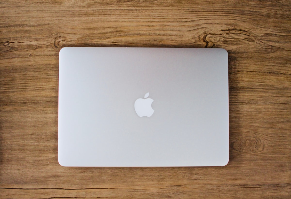 木製のデスクに置かれた閉じたMacBookを真上から写したイメージ画像