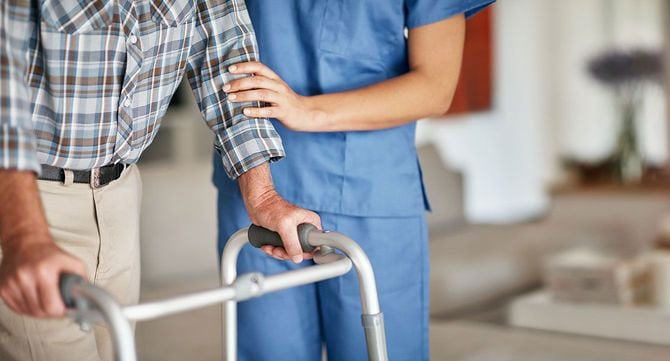 歩行器を使う高齢男性を介助する介護スタッフ