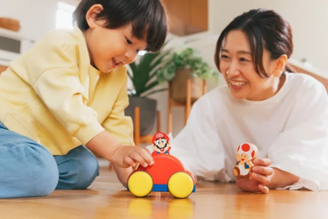のせかえメロディーカーで遊ぶ子どもと、キノピオのつみきを持つ女性