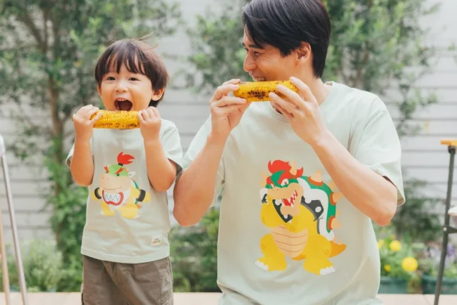クッパとクッパJr.のTシャツを着た親子がとうもろこしを食べている