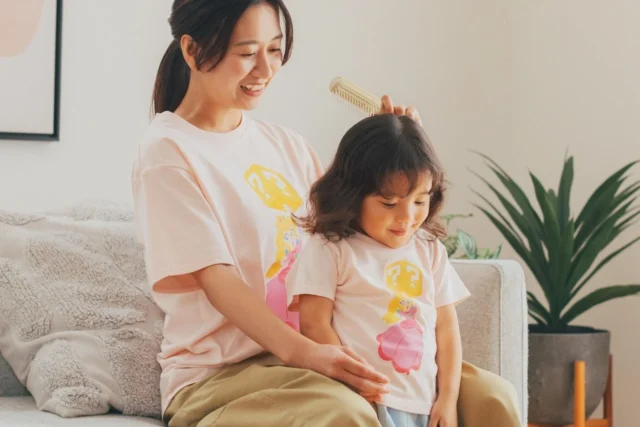 ピーチのアパレルTシャツを着た親子がソファで髪をとかす様子