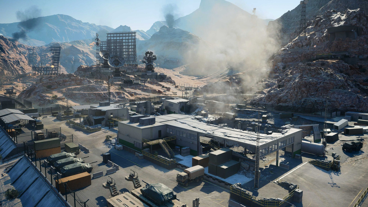 『Battlefield 6』「Area 51」のスクリーンショット。岩山に囲まれた基地を見下ろす構図で、手前に覆いを掛けた車両が並び、奥にパラボラアンテナと鉄塔が建つ