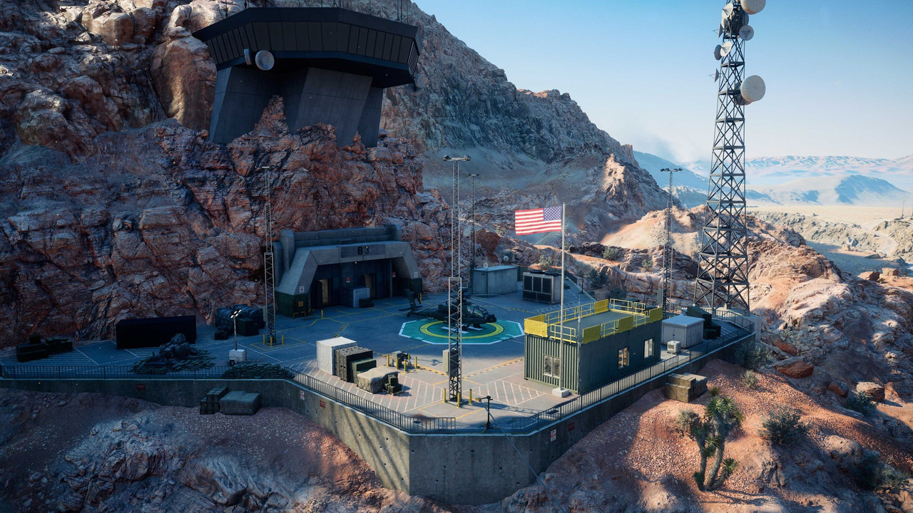 『Battlefield 6』「Area 51」のスクリーンショット。岩壁に張り出した監視施設の下に、星条旗が掲げられたヘリポートと鉄塔がある