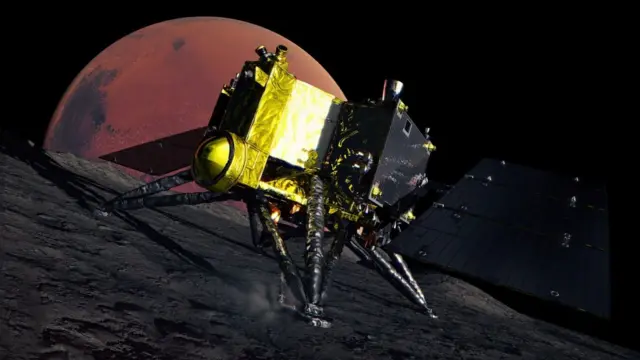 金と黒の探査機が宇宙空間で、岩の表面に着陸している。探査機は4本の三角形の脚と暗い色の太陽電池パネルを備えている。背景には火星の赤い円盤が見える